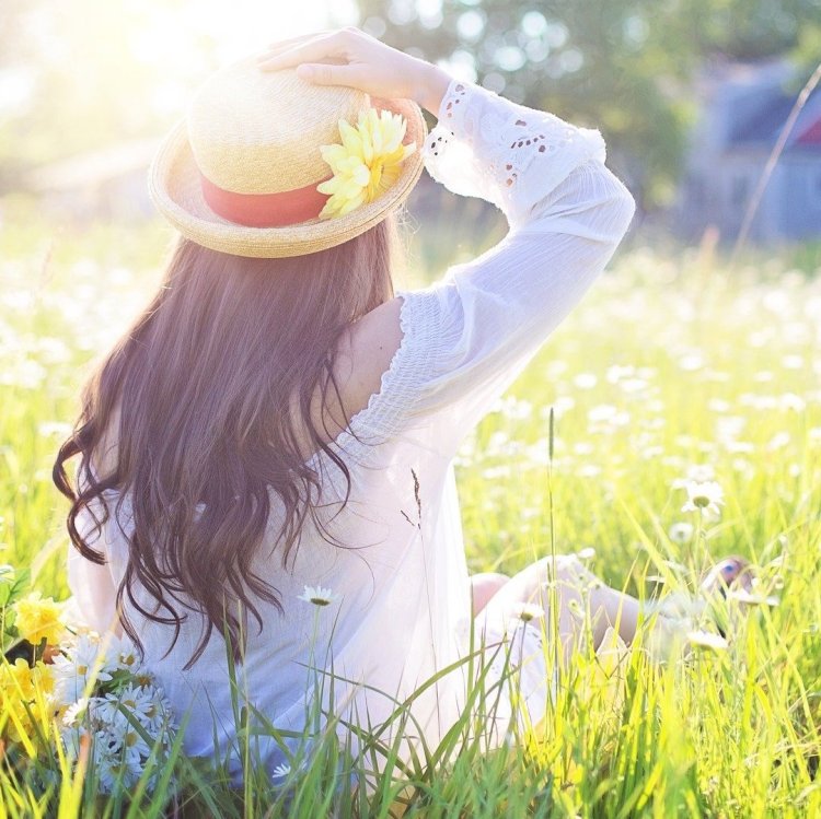 Photo d'une jeune fille de dos, assise dans l'herbe au soleil